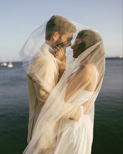 Casal sob um véu de noiva à beira do mar
